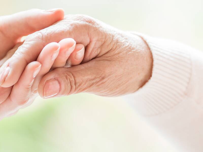 Zwei Hände halten einander sanft, wobei eine Hand jünger und die andere älter ist.