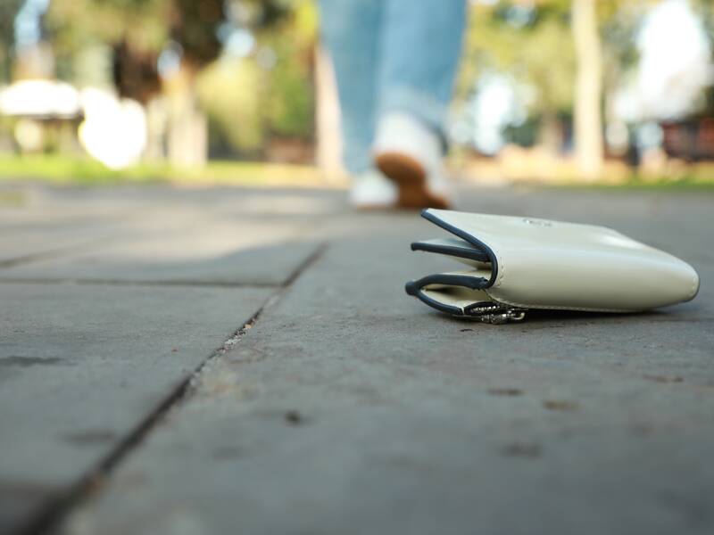 Ein weißer Geldbeutel liegt auf der Straße und im Hintergrund sieht man eine Person mit weißen Schuhen weglaufen