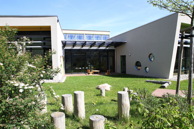 Das Bild zeigt einen Garten mit Sitzmöglichkeiten aus Holz und blauem Himmel im Hintergrund