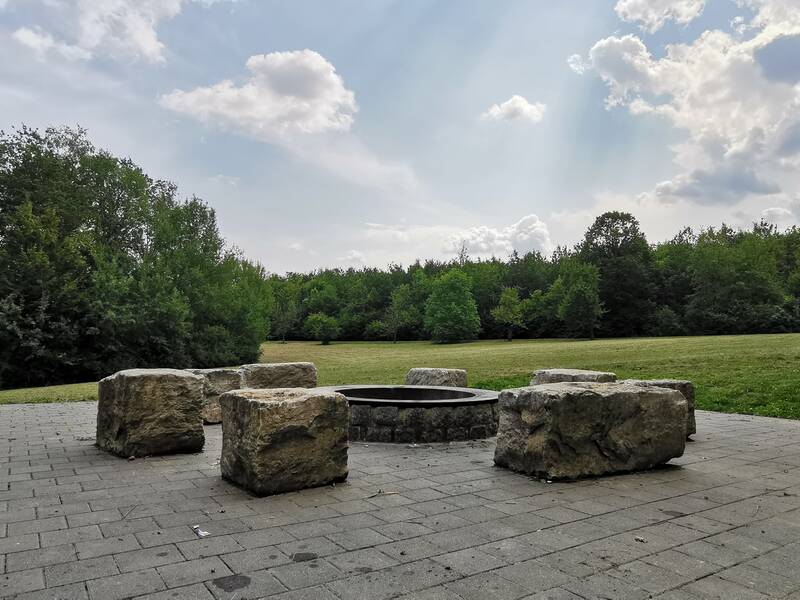 Das Bild zeigt eine Grillstelle mit großen Sitzsteinen und einem Wald im Hintergrund