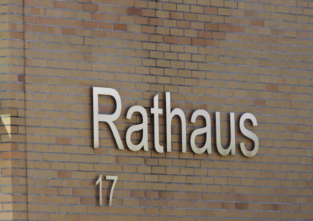 Die Fassade eines Gebäudes zeigt das Wort "Rathaus" und die Nummer "17" in großen Buchstaben auf einer Ziegelmauer.