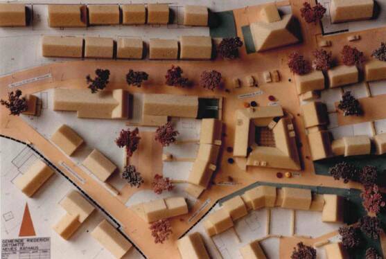 Das Bild zeigt ein architektonisches Modell einer städtischen Planung mit Gebäuden, Straßen und Bäumen.